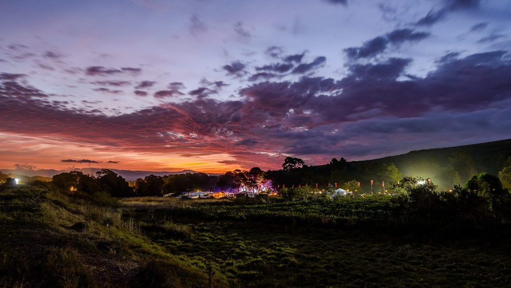 Sunset over the festival site, with the stage lights coming on below a red and purple sky